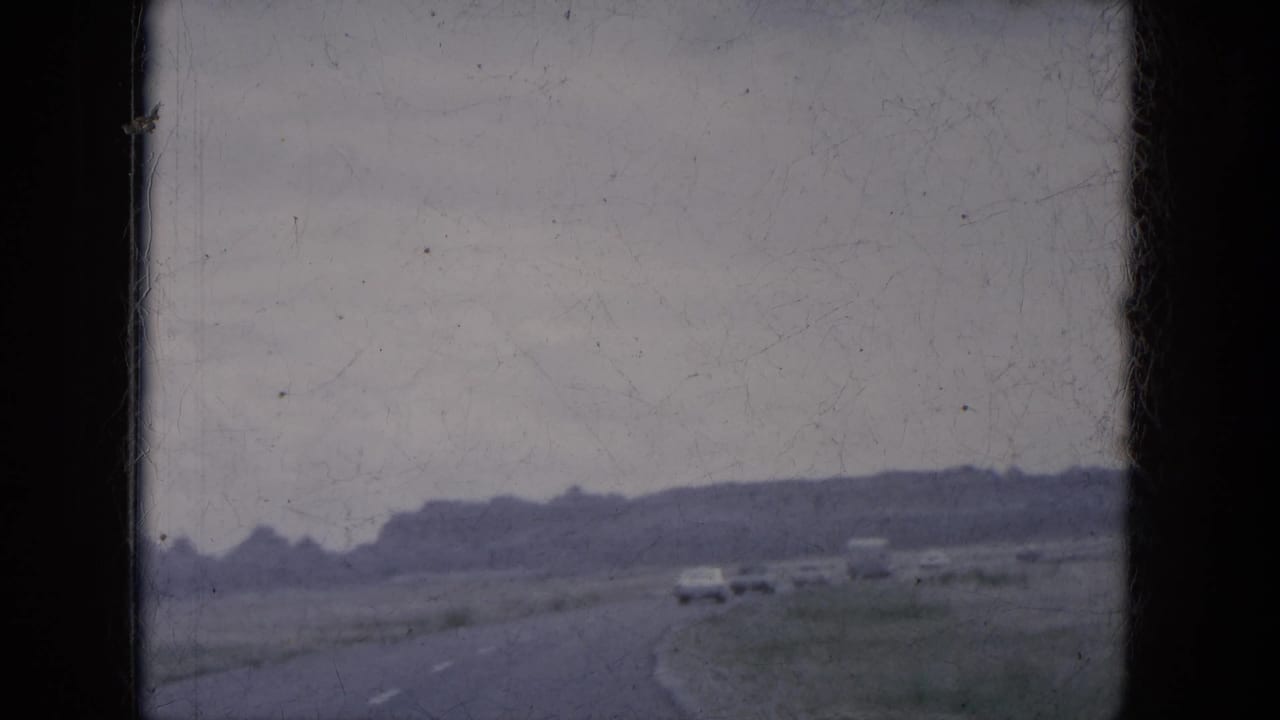 Flat open road curving through low hills with several cars ahead under a cloudy sky.