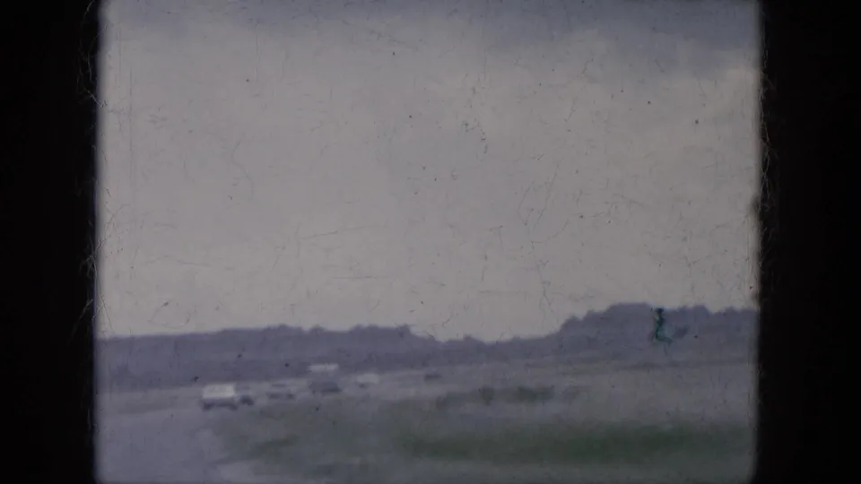 Weathered 1969 home-movie frame from a moving vehicle, showing cars on an open Arizona road with soft focus and visible film wear.