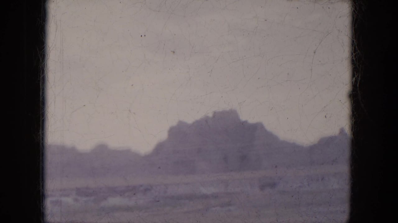 Distant desert hills seen through dark car-window framing on aged 8mm film.
