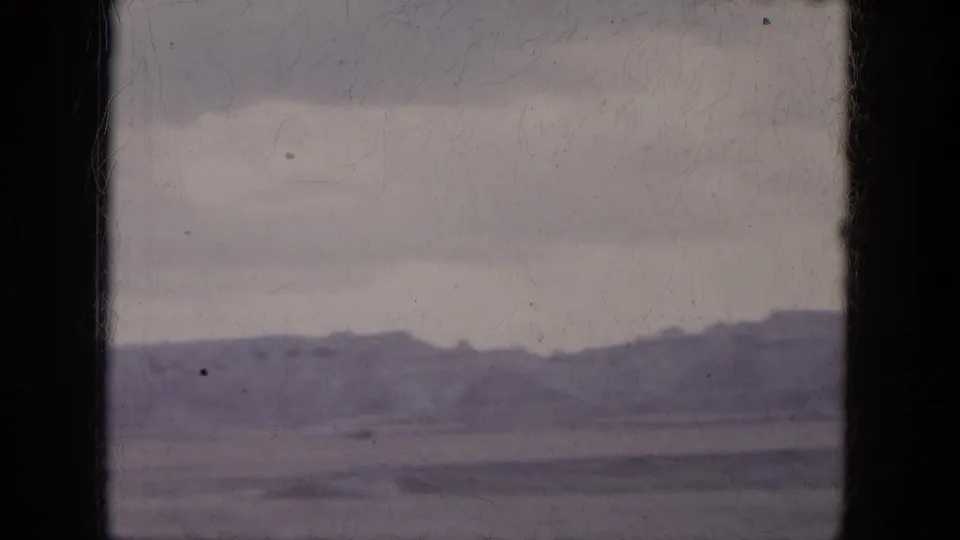 1969 home-movie frame showing low Arizona desert hills beneath a pale sky from a passenger-window viewpoint.