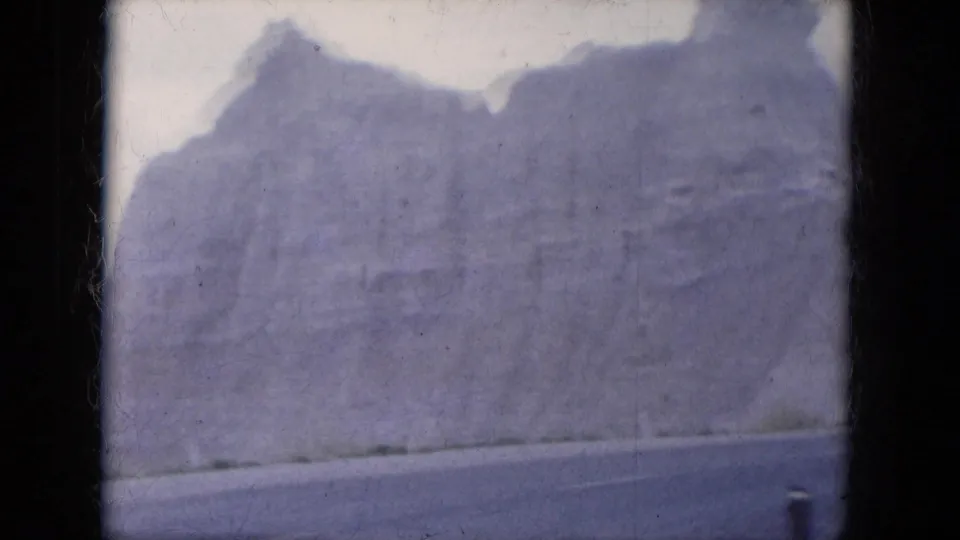 Faded 8mm view of a large Lake Canyon rock wall, with a road edge at the bottom and soft hazy exposure.