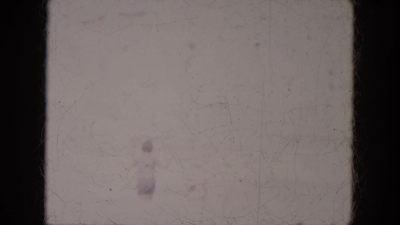 Faded 8mm frame with a faint figure on pale open ground.