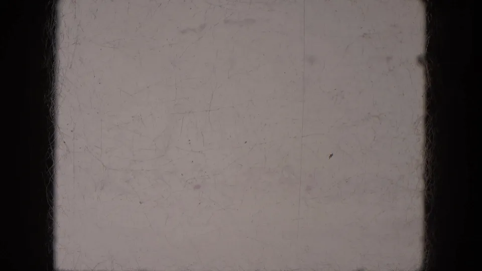 Off-white 8mm blank frame from the supplied 1969 Lake Canyon clip, showing dark borders, dust flecks, scratches, and slight tonal variation.