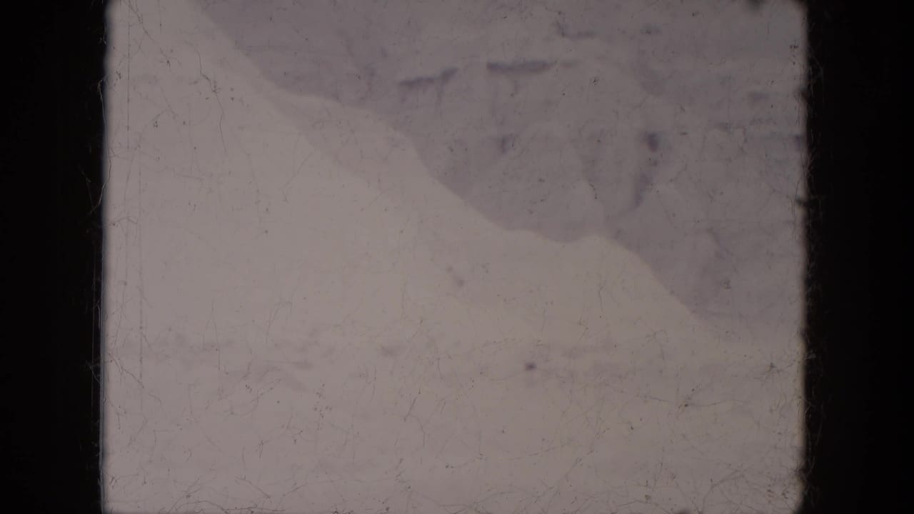 Pale snowy scene with faint distant marks, dark film borders, scratches, and dust.