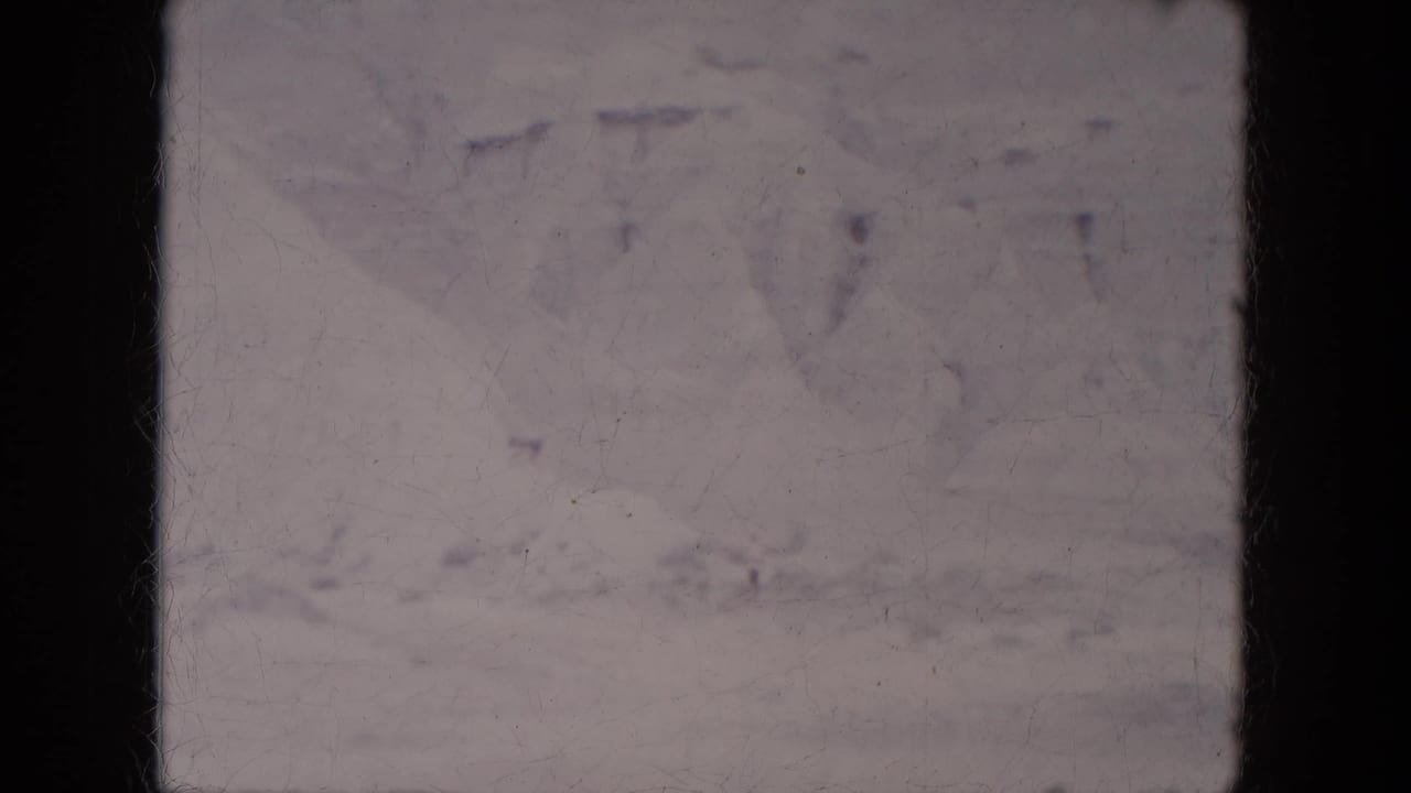 Faint snowy mountain landscape under a pale sky with dark film-frame edges.