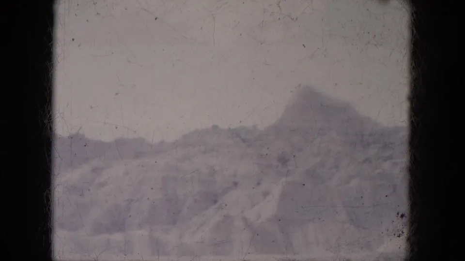1969 8mm Lake Canyon landscape with distant rugged mountains, snow patches, pale sky, and soft home-movie color.