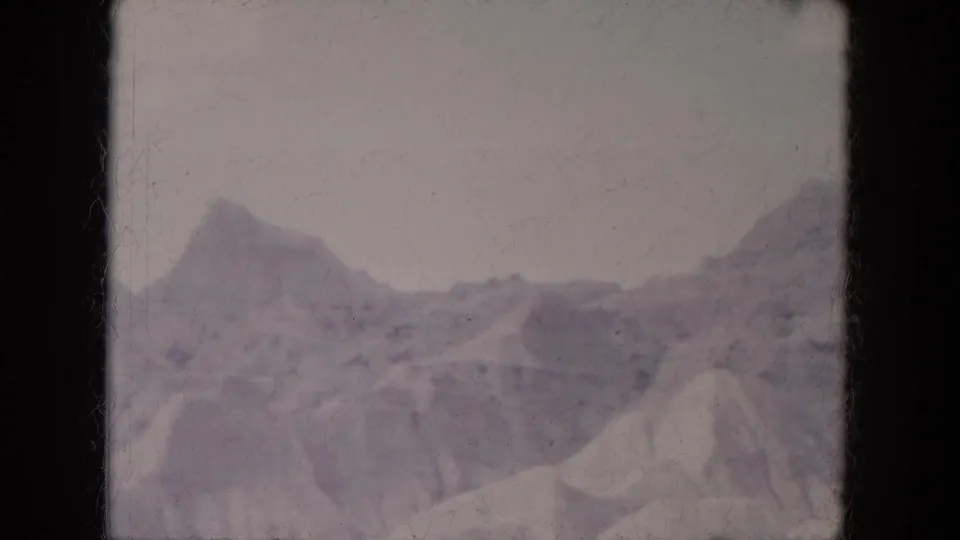 1969 Lake Canyon 8mm frame showing snow-streaked ridges, a pale sunny sky, muted color, and film-edge darkness.