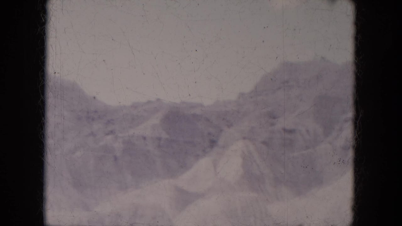 Distant snow-covered mountain ridge above pale open terrain in a soft 8mm frame.