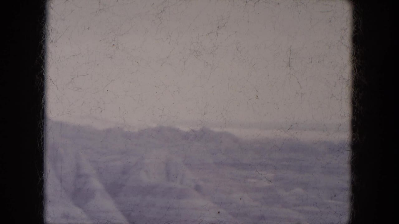 1969 Lake Canyon, Arizona home-movie frame showing distant rocky hills beneath a pale sky with visible 8mm border and dust.