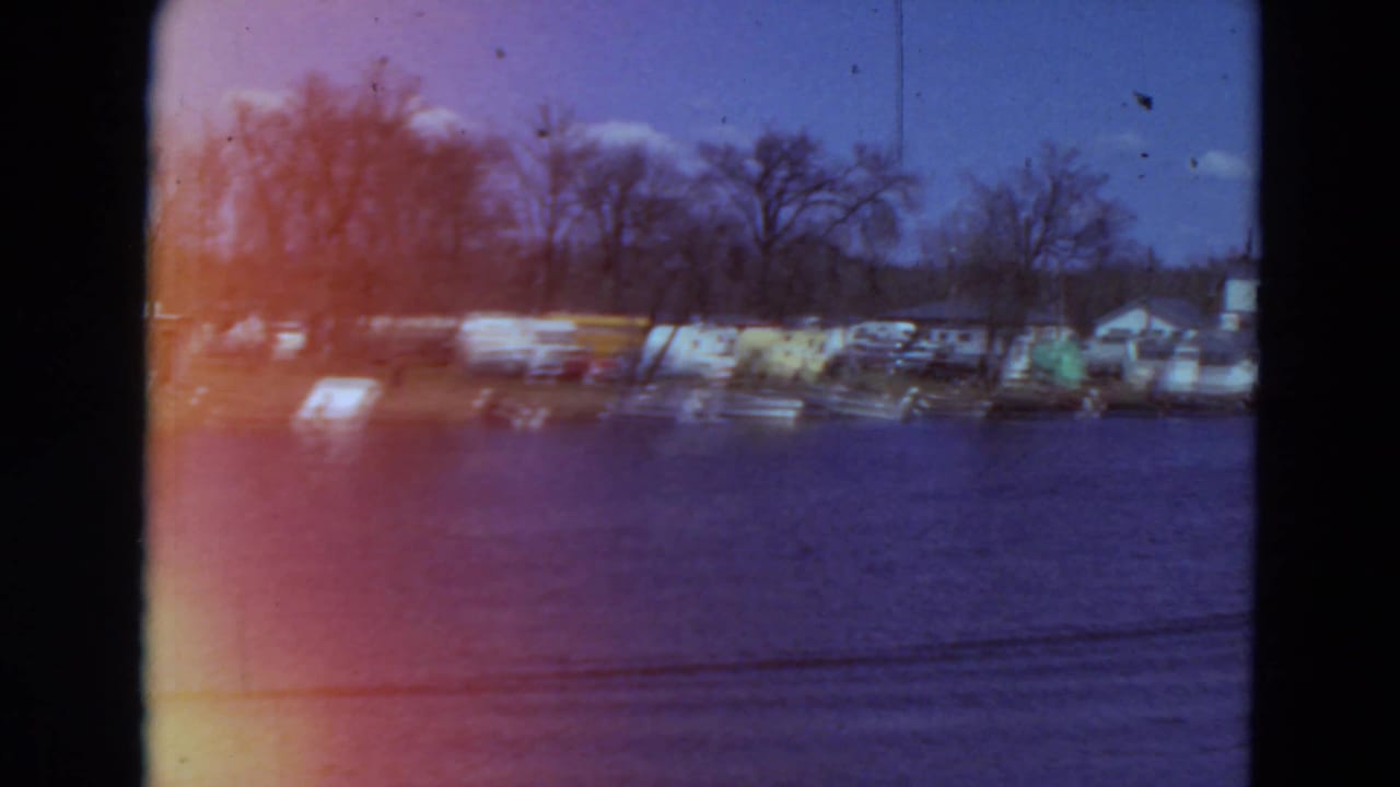 Lakeside shoreline with boats, parked cars, bare trees, and dark film gate edges.