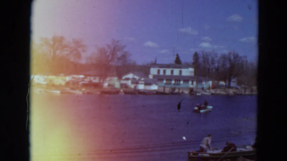 1969 Minnesota lake scene with shoreline boats, modest buildings, leafless trees, and people in small craft near the foreground edge.