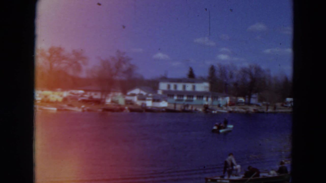 Lakeside building and parked cars across the water, with a small boat near the foreground.