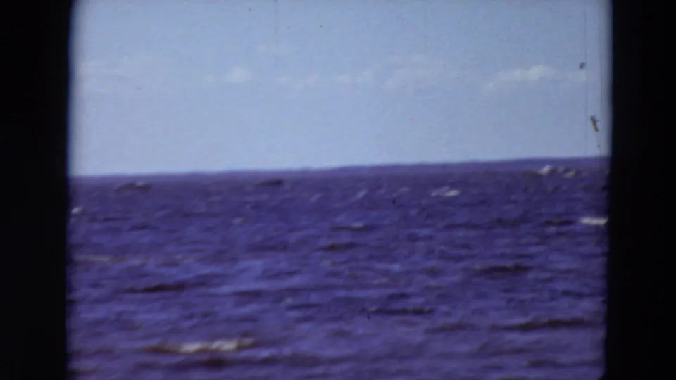 1969 Minnesota 8mm frame of rippling river water and a low distant shoreline under a pale sky.