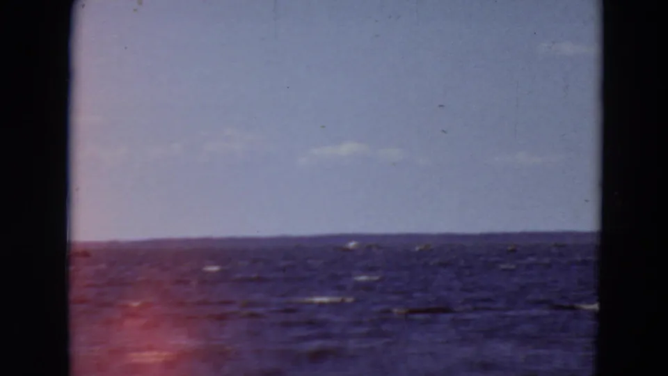 1969 Minnesota 8mm frame of rippled open water and pale sky, marked by a red light leak near the lower left edge.