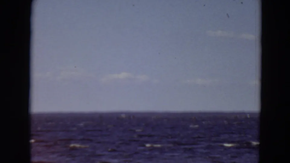 1969 Minnesota 8mm frame with blue open water, small wave highlights, pale clouds, and a low horizon line.