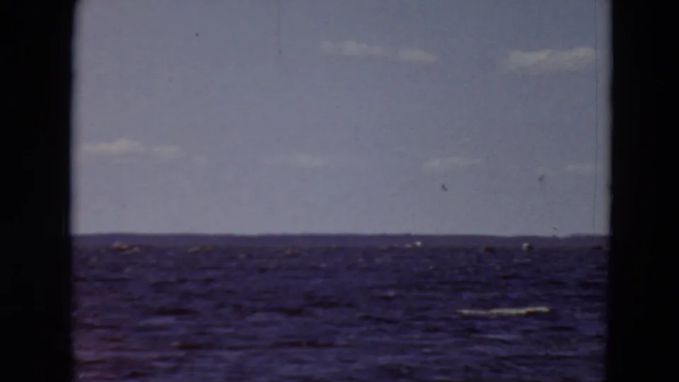 1969 Minnesota 8mm frame showing a distant low shoreline across rippled blue water under a lightly clouded sky.