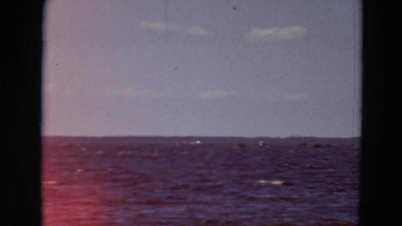 Open blue-purple water under a pale sky, framed by dark film or window edges.