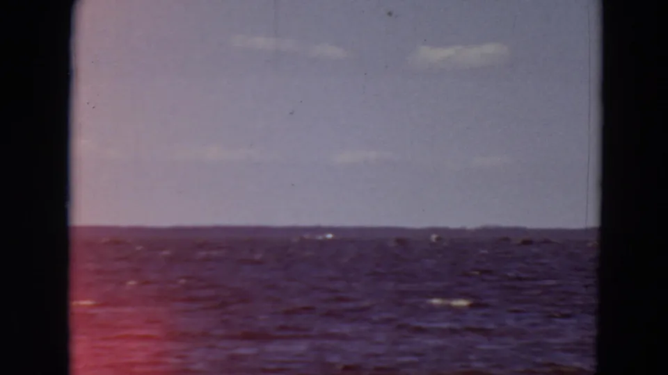 1969 Minnesota 8mm frame showing open water, distant low horizon, pale sky, and dark vertical framing edges.