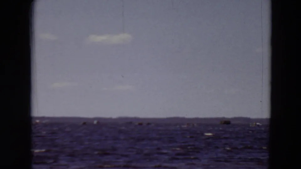 1969 Minnesota 8mm frame showing textured water, a low distant horizon, pale sky, and soft home-movie color shifts.
