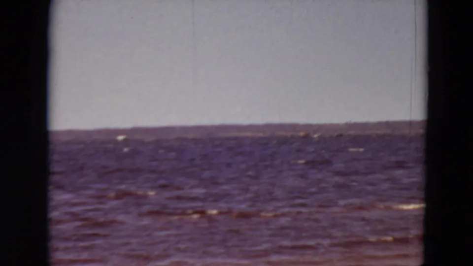 1969 Minnesota 8mm frame with choppy lake surface, small whitecaps, pale sky, and distant shore softened by film grain.
