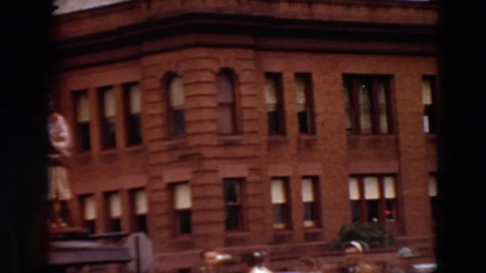 Minnesota 1969 home-movie frame of a brick urban building with rows of windows and a partially framed rooftop statue.