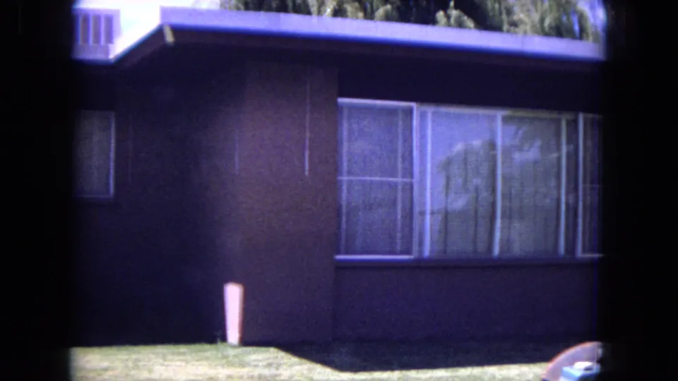1970 White Sands, Florida home-movie frame showing large windows, dark siding, and lawn moments before the yard work action enters.