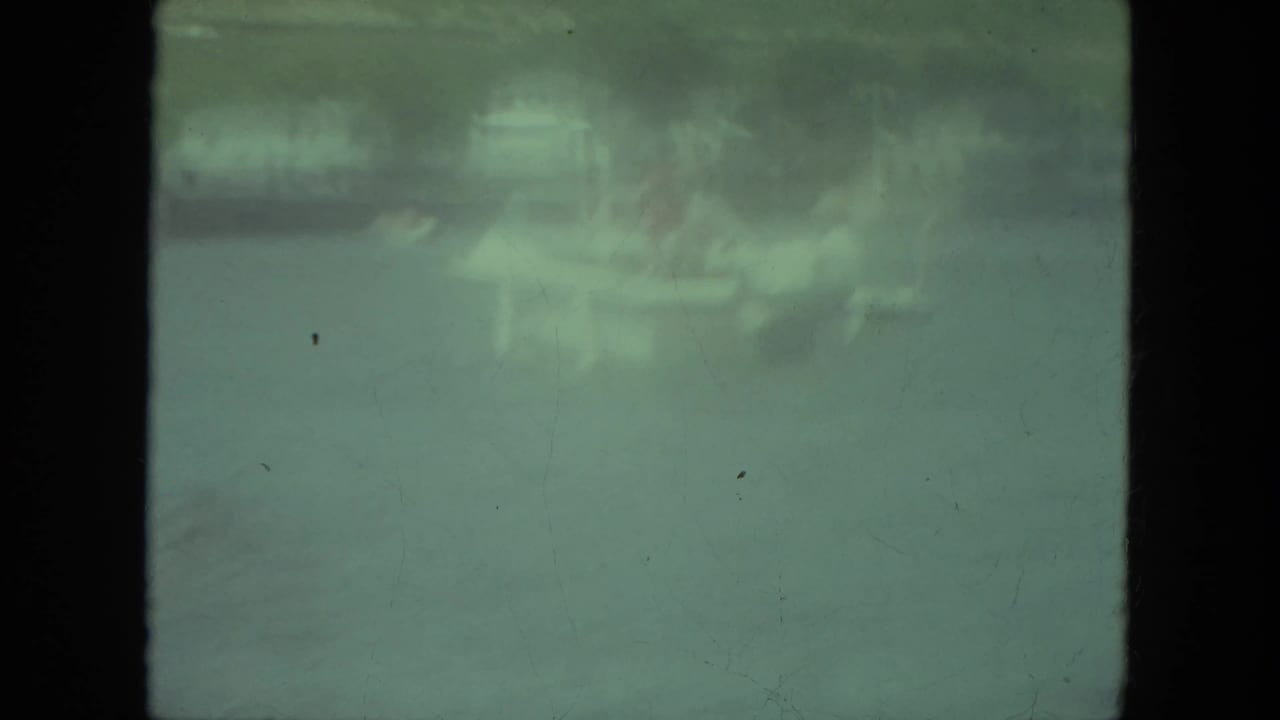 1971 Mississippi home-movie frame showing two adult men in a small boat on calm lake water, with details softened by film color shift.