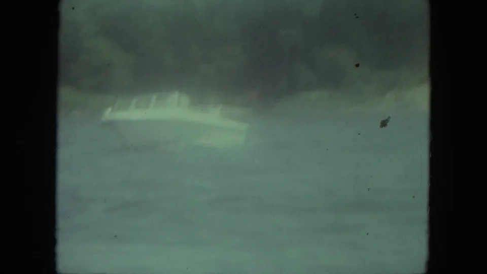 1971 Mississippi home-movie frame with two men in a small boat on lake water, seen through heavy softness, grain, and green color shift.