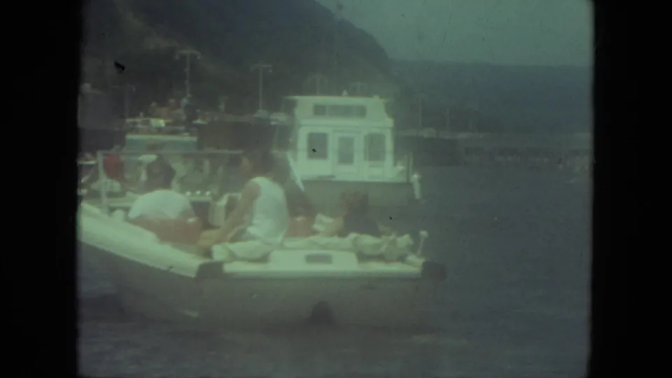 1971 Mississippi-labeled frame of people seated in a small white boat with a larger vessel and wooded shoreline behind them.