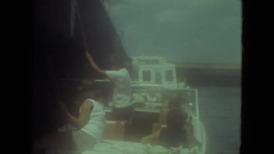 1971 Mississippi River frame showing a man at the stern of a small boat, seated passengers, rigging, and a larger vessel in the background.
