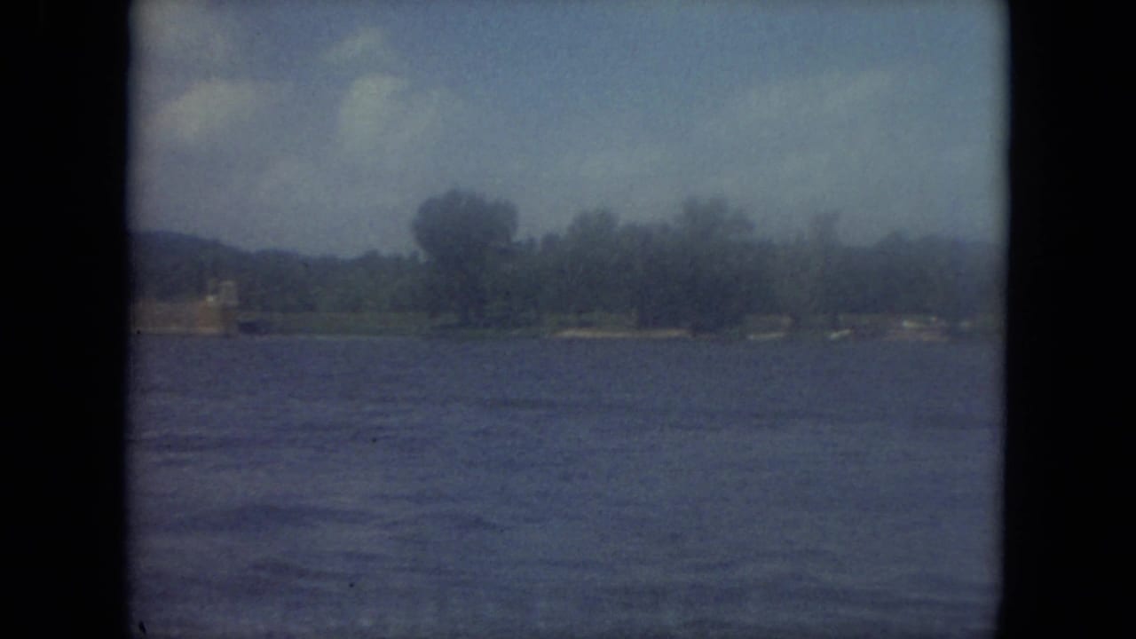 1971 Mississippi 8mm frame showing lake water, far shoreline trees, low hills, and hazy sky before the boat enters view.