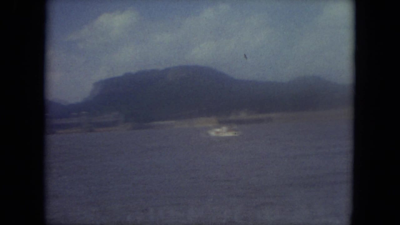 Soft 8mm view across a Mississippi lake toward low hills, with a small distant wake visible on the water.