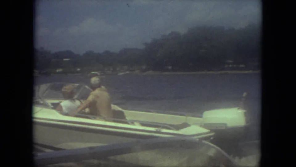 1971 Mississippi home-movie frame of a small open speedboat carrying three people across the lake near the camera.