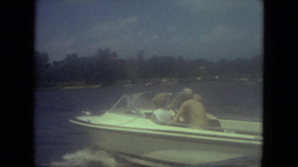 Small speedboat with three visible passengers cruises across a Mississippi lake in soft, grainy 8mm color footage.