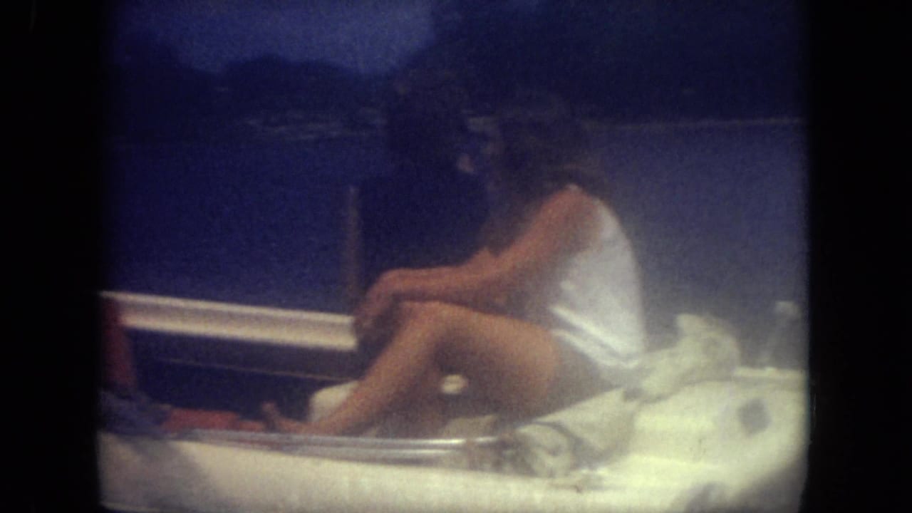 Two people seated in a small boat on a lake, seen through soft blue-tinted 8mm film.