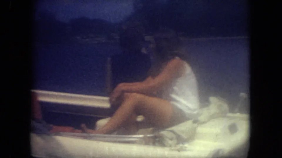 1971 Mississippi home-movie frame showing people in swimwear seated close together in a small boat on lake water.