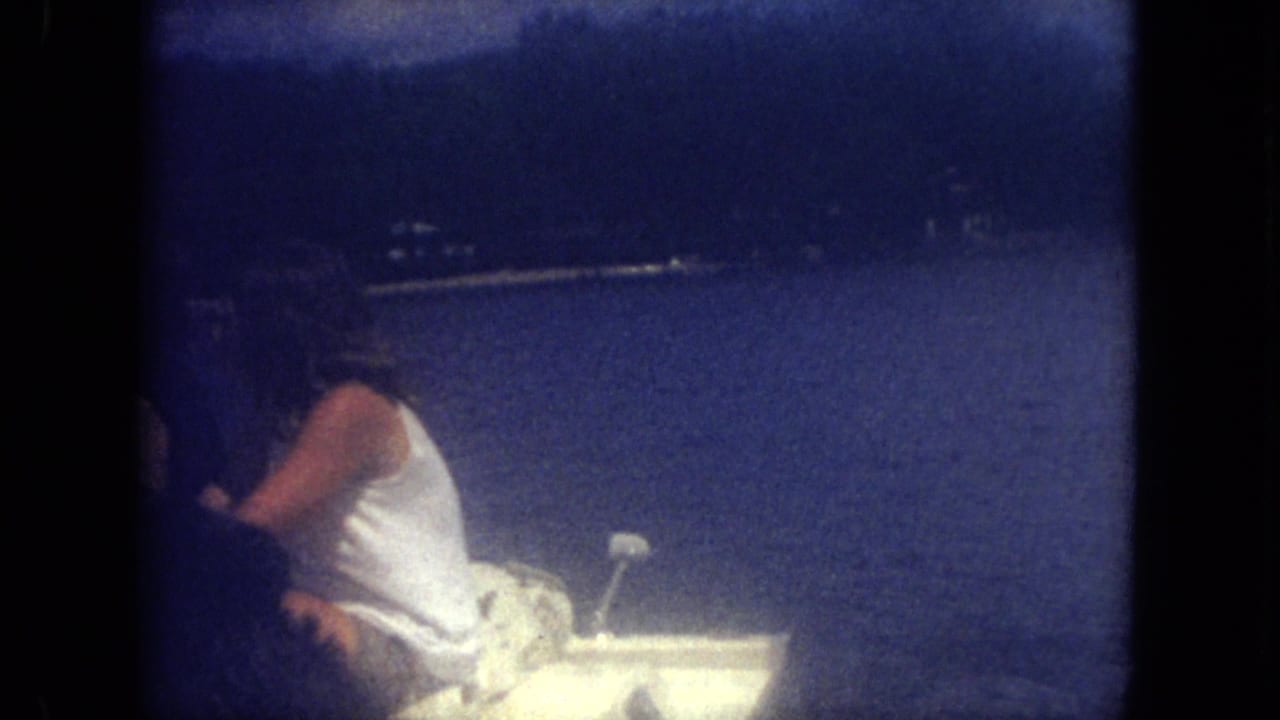 1971 Mississippi lake scene with a person seated in a small white motorboat, filmed in soft blue 8mm color.
