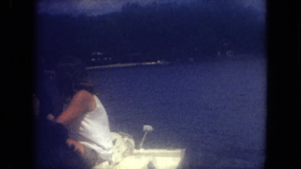 1971 Mississippi lake scene with a person seated in a small white motorboat, filmed in soft blue 8mm color.