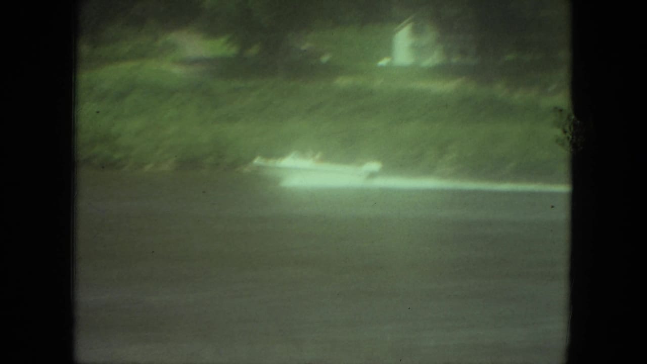 1971 Mississippi 8mm frame with a small speedboat crossing a river, white wake trailing near a soft green shoreline.