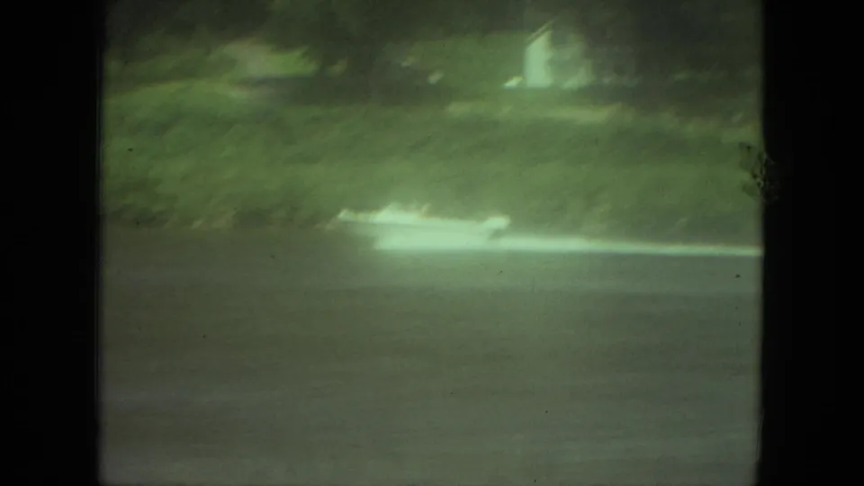 1971 Mississippi 8mm frame with a small speedboat crossing a river, white wake trailing near a soft green shoreline.