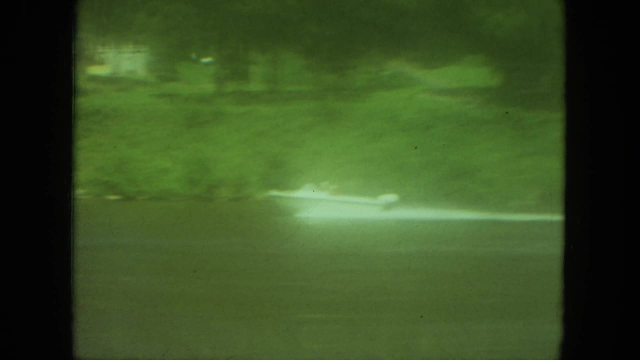 Green-tinted 1971 Mississippi river view with a small speedboat and long white wake against trees and grass.