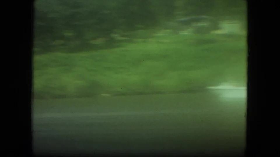 Motion-blurred 8mm Mississippi riverbank frame with grass, trees, river water, and the speedboat wake partly visible.