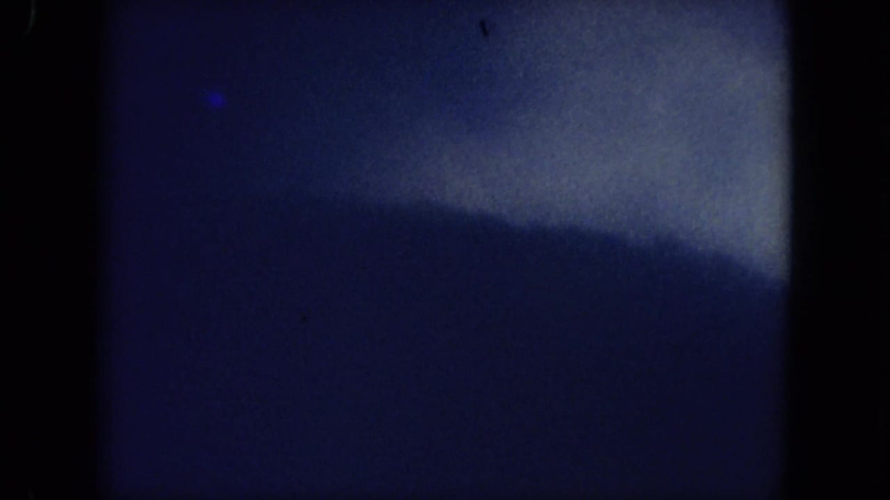 Mississippi 1971 home-movie frame showing calm water and a distant tree line with heavy grain and soft exposure.