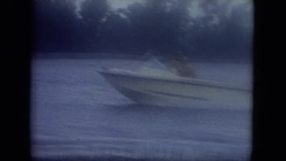 1971 Mississippi 8mm frame showing a small speedboat gliding across a canal with a visible wake and dark shoreline trees.