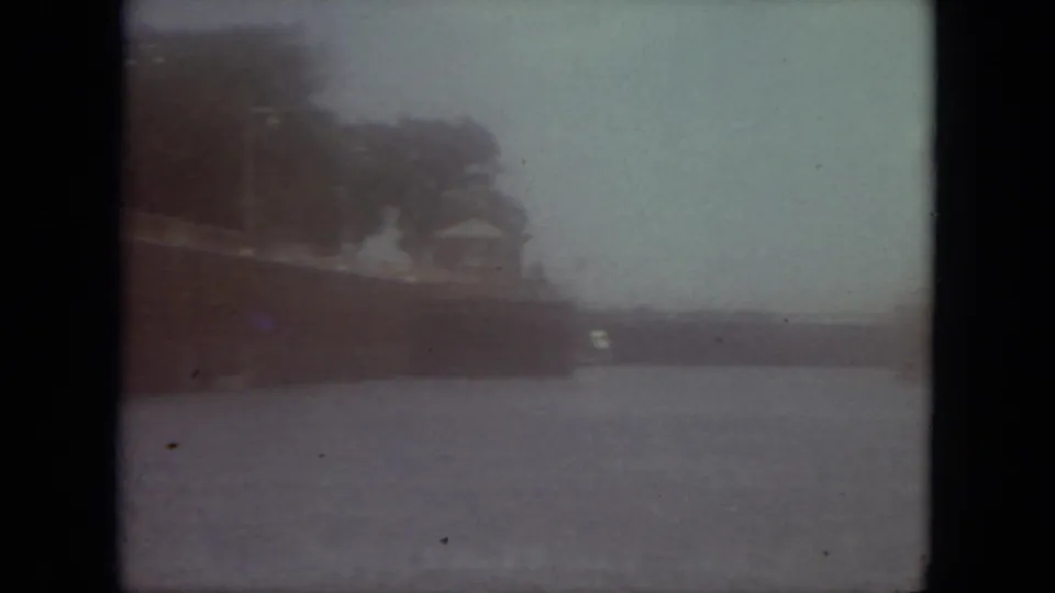Hazy 8mm waterfront shot in Mississippi, with a distant shoreline and ship-like form across the water.