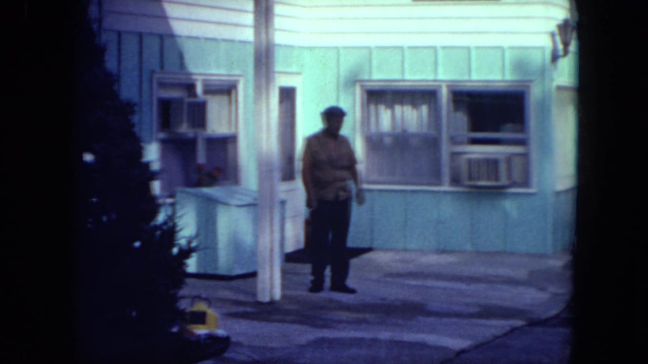 Man standing outside a light blue motel room with an open doorway and window air conditioner.