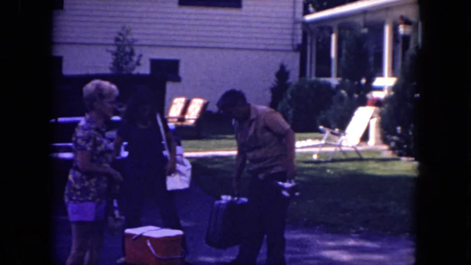 Two women and a man stand near luggage and a cooler beside a vehicle in the Mississippi motel yard.