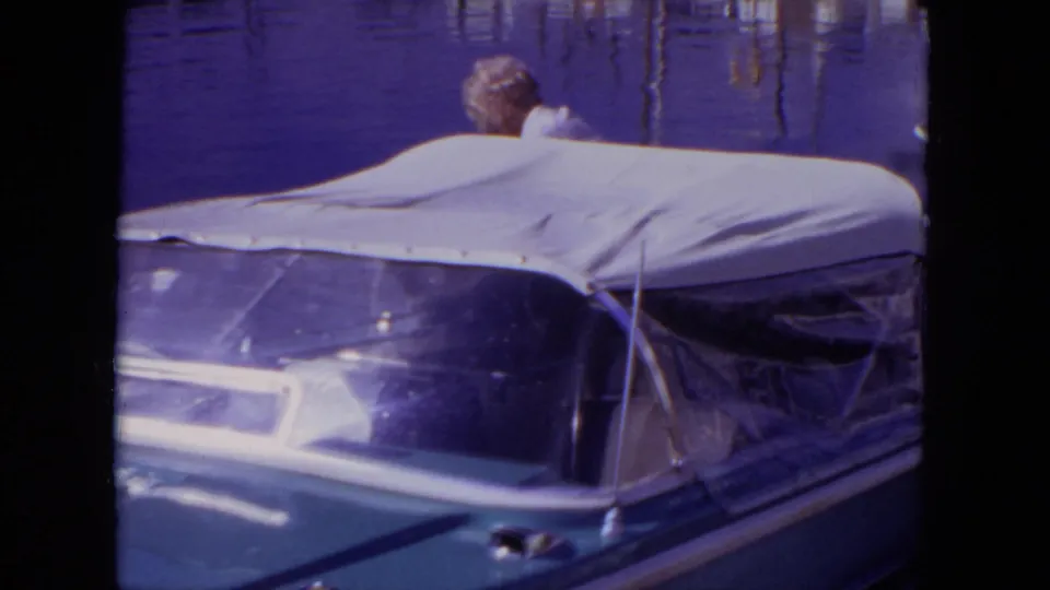 1971 Mississippi marina frame with a canvas-covered motorboat in front and a partly visible adult near the water behind it.