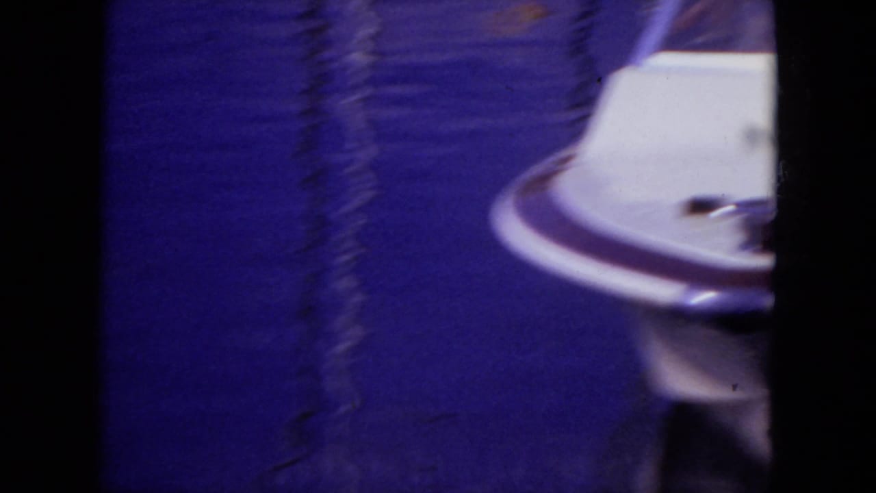 A soft, motion-blurred 1971 Mississippi 8mm frame shows part of a white speed boat moving across blue lake water.