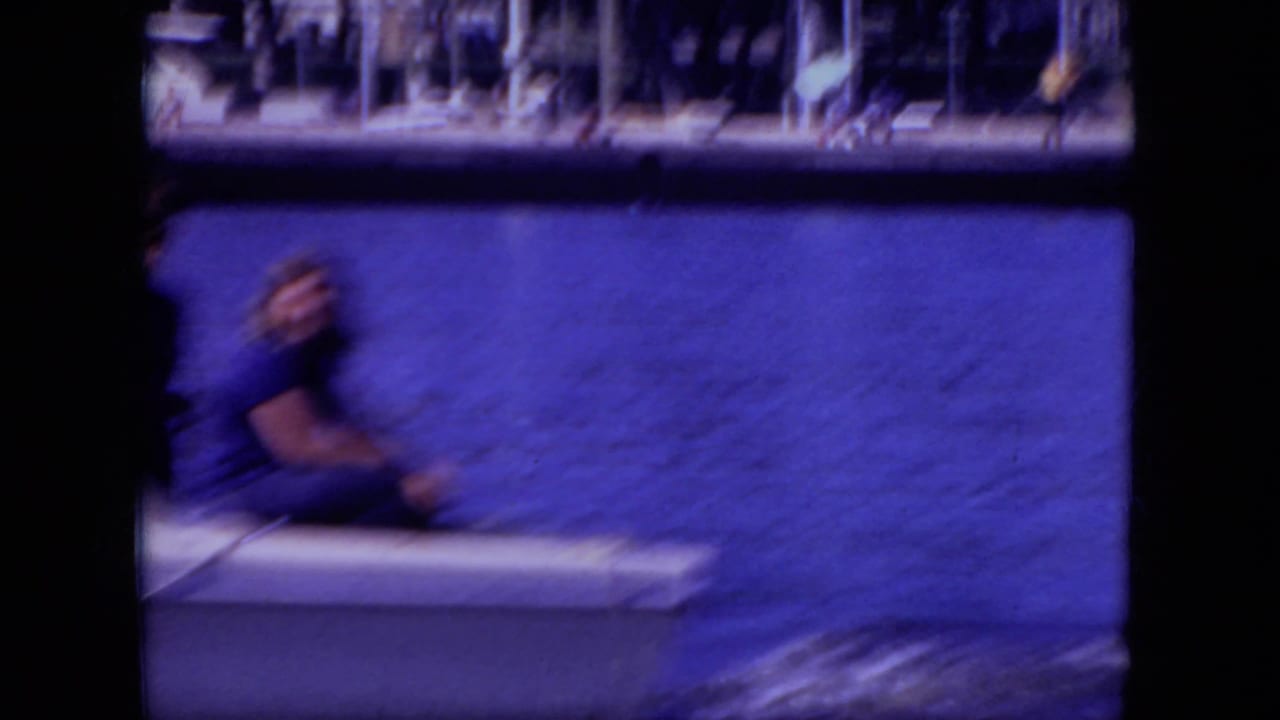 Young person seated at the back of a white boat on blue water near a distant shoreline.